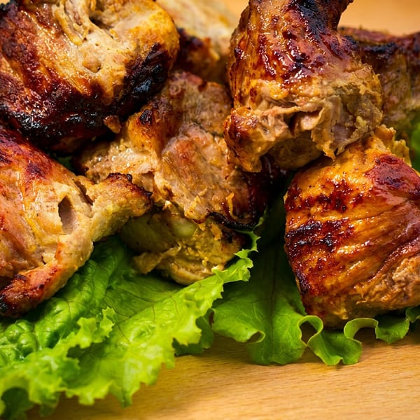 Golden brown grilled meat pieces resting on fresh green lettuce leaves.
