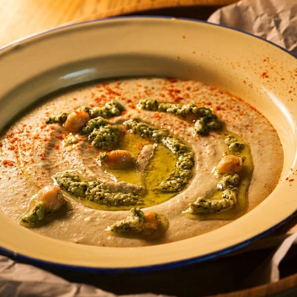 Creamy hummus with green pesto, chickpeas, olive oil, and paprika, served with pita bread.