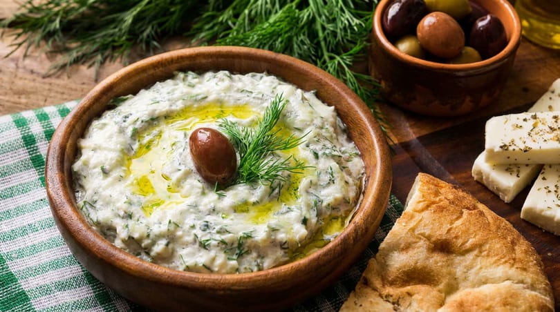 Mediterranean spread featuring a creamy dip, pita bread, feta cheese, and olives.