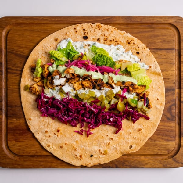 Open chicken wrap with lettuce, red cabbage, pickles, and sauces on a wooden board.