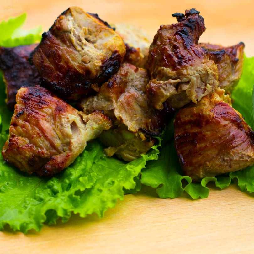 Grilled meat pieces with a crispy brown crust, served on fresh green lettuce leaves.