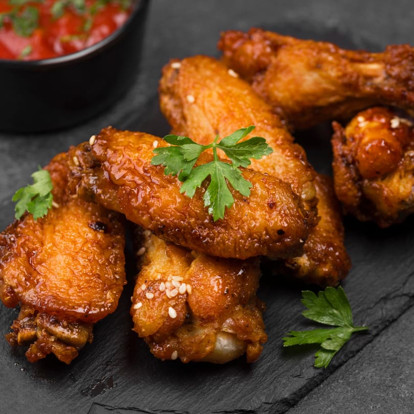 Crispy glazed chicken wings with sesame seeds and parsley, served with a red dipping sauce.