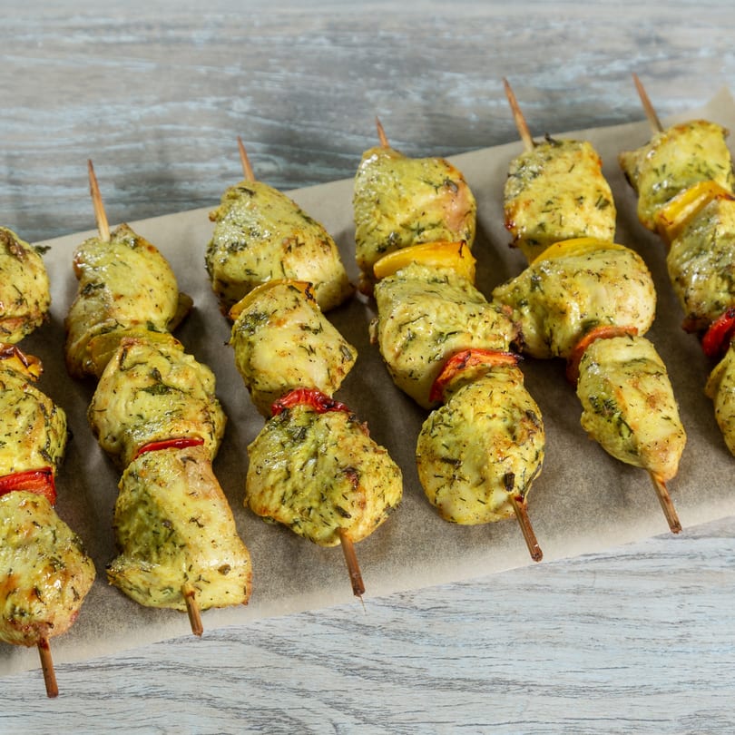 Rows of chicken and vegetable skewers with yellow and red bell peppers on parchment paper.