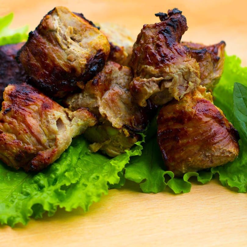 Grilled meat pieces with a crispy brown crust, served on fresh green lettuce leaves.